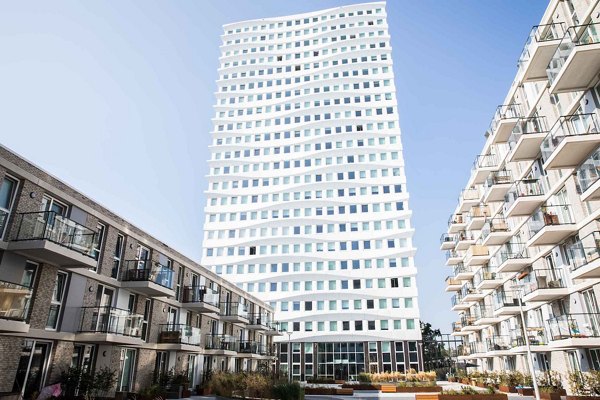 Contemporary architecture with a striking white high-rise building contrasting with multi-story residential units, set against a clear blue sky.
