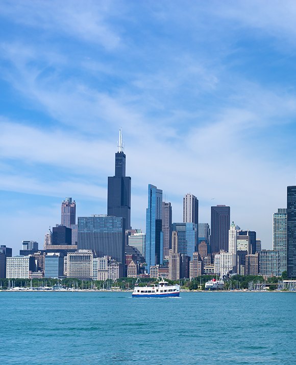 A panoramic view of a bustling city skyline with a prominent bridge over a blue body of water, under a clear sky.